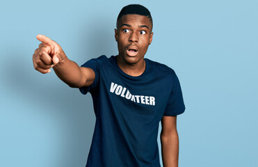 Young african american man wearing volunteer t shirt pointing with finger surprised ahead, open mouth amazed expression, something on the front