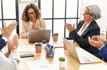 Group of middle age business workers smiling and clapping to partner at the office.