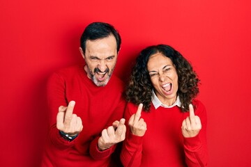 Middle age couple of hispanic woman and man hugging and standing together showing middle finger...