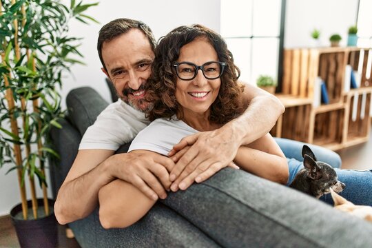 Middle age hispanic couple smiling happy sitting on the sofa with dogs at home.