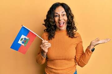 Middle age hispanic woman holding haiti flag celebrating achievement with happy smile and winner expression with raised hand