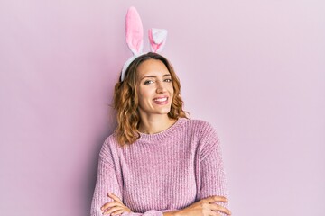 Young caucasian woman wearing cute easter bunny ears happy face smiling with crossed arms looking...