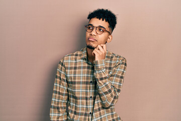 Young african american man wearing casual clothes and glasses serious face thinking about question with hand on chin, thoughtful about confusing idea