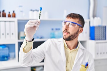 Young hispanic man wearing scientist uniform holding test tube at laboratory