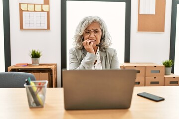 Middle age businesswoman sitting on desk working using laptop at office looking stressed and...