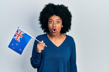 Young african american woman holding new zealand flag scared and amazed with open mouth for surprise, disbelief face