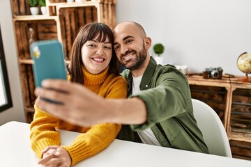 Young hispanic couple smiling happy make selfie by the smartphone sitting on the table at home.