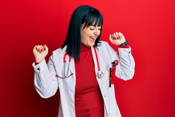 Young hispanic woman wearing doctor uniform and stethoscope dancing happy and cheerful, smiling moving casual and confident listening to music