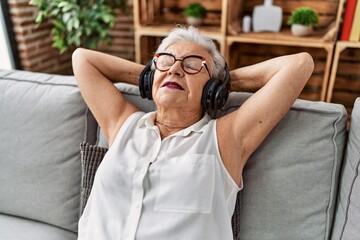 Senior grey-haired woman listening to music sitting on sofa at home