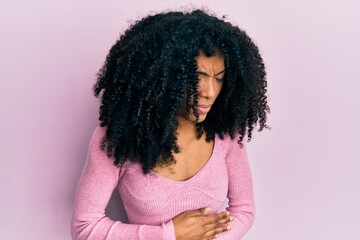 African american woman with afro hair wearing casual pink shirt with hand on stomach because indigestion, painful illness feeling unwell. ache concept.