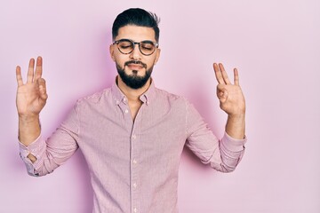 Fototapeta premium Handsome man with beard wearing casual shirt and glasses relax and smiling with eyes closed doing meditation gesture with fingers. yoga concept.