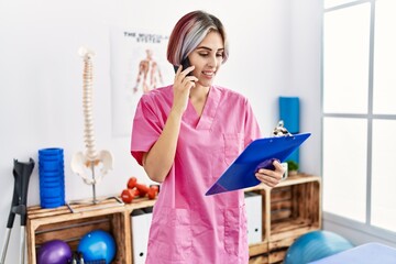 Young caucasian physiotherapist smiling happy talking on the smartphone at the clinic.