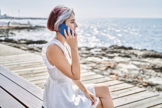 Young caucasian girl talking on the smartphone sitting on the bench at the beach.