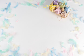 Easter colored eggs in a box, on a white background decorated with colored feathers. There is space for text. View from above.