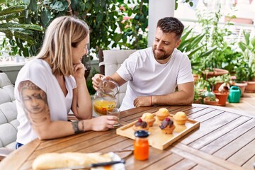 Young couple having breakfast pouring jar with juice at terrace.