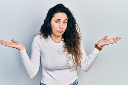 Young hispanic woman wearing casual clothes clueless and confused with open arms, no idea and doubtful face.
