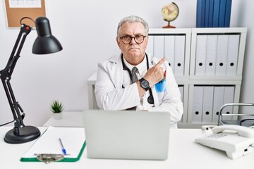 Obraz premium Senior caucasian man wearing doctor uniform and stethoscope at the clinic pointing with hand finger to the side showing advertisement, serious and calm face