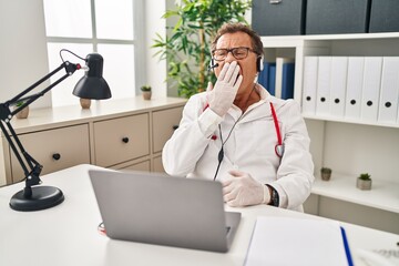 Senior doctor man working on online appointment bored yawning tired covering mouth with hand. restless and sleepiness.