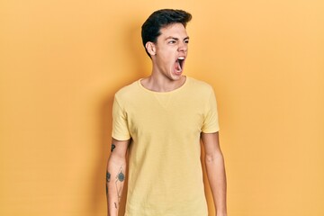 Young hispanic man wearing casual yellow t shirt angry and mad screaming frustrated and furious,...