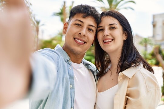 Young hispanic couple of boyfriend and girlfriend together outdoors on a sunny day, smiling in love taking a selfie picture
