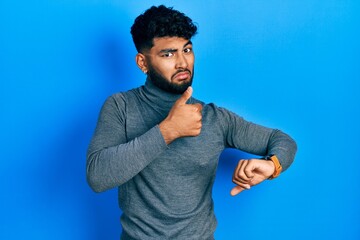 Arab man with beard wearing turtleneck sweater doing thumbs up and down, disagreement and agreement expression. crazy conflict