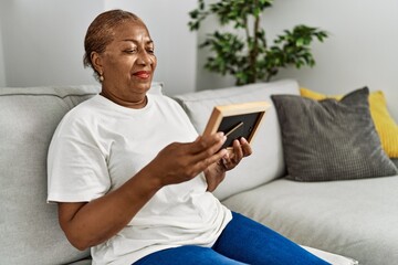 Senior african american woman looking photo sitting on sofa at home