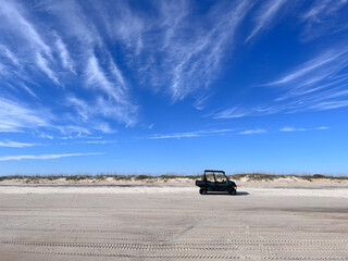 An ATV sits on the sand of a beach on the Outer Banks of North Carolina under a blue sky with...