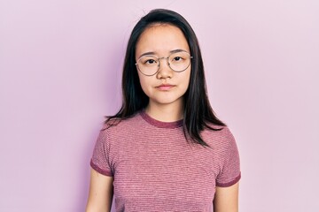 Fototapeta premium Young chinese girl wearing casual clothes and glasses relaxed with serious expression on face. simple and natural looking at the camera.