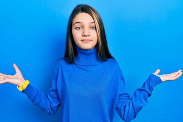 Young brunette girl wearing turtleneck sweater clueless and confused expression with arms and hands...