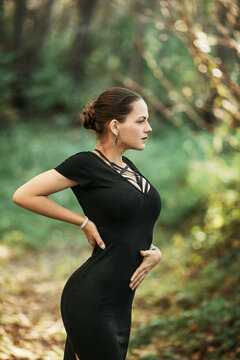 Sensual woman with bondage and in a black dress, posing in front of a summer forest