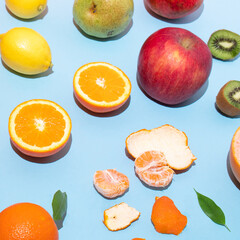 Blue background and fresh fruit on it. Orange, tangerine and kiwi cut in half, red apple, orange, lemon, green leaf. Creative summer concept.