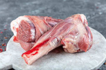 Fresh raw meat of leg young lamb. Raw lamb leg on marble stone background with herbs.