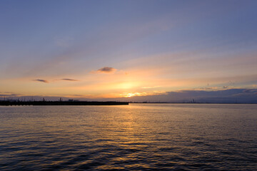 早朝、朝日にキラキラ輝き、黄金色に輝く海。兵庫県芦屋市芦屋浜より大阪湾を臨む。遠くに大阪南港のビルが見える