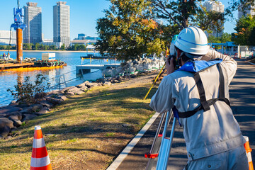 Surveyor at work. Topographic survey of embankment. Man with surveying equipment. Man with optical theodolite. Surveyor on embankment. Geodetic studies of bay. Topography of Tokyo. Japan Geodesy