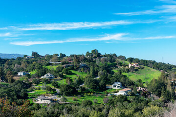 Fototapeta na wymiar Row of solar panels. Background upscale hillside homes in suburban residential neighborhood on green hills under blue sky