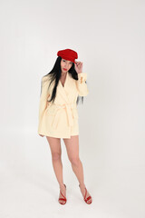 Stylish fashionable brunette woman in a yellow jacket, red cap and beautiful legs in the studio on a white background