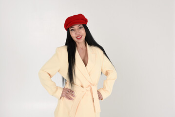 Stylish fashionable brunette woman in a yellow jacket and a red cap in the studio on a white background with a smile