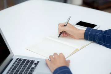 Closeup hand of business man writing on note while using laptop computer on desk at home, male planning on note for business success, author and blog, businessman working on table, employee and job.