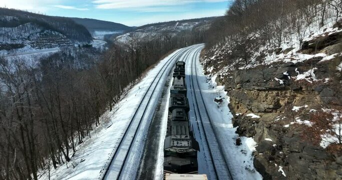 Train engine locomotive pulls railcars through snowy mountain pass in winter. Beautiful scenic aerial.