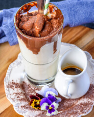 A serving of iced coffee in a tall glass with ice cream and chocolate powder