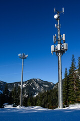 Wireless cell site with antenna mounted on towers in a winter mountain landscape on a sunny day.
