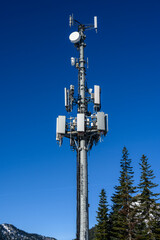 Wireless cell site with antenna mounted on towers in a winter mountain landscape on a sunny day.
