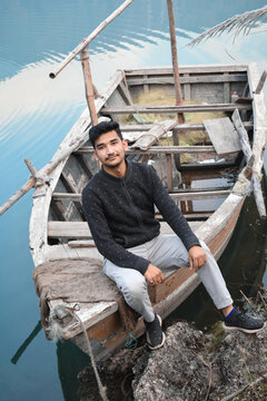Guy sitting on fishing boat on shore posing for photo