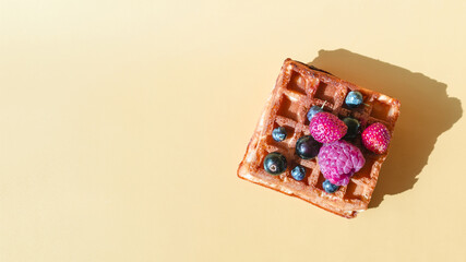 Soft waffle with a decor of black and red berries on a yellow background natural hard light.
