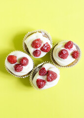Cupcakes with white cream and red berries on a yellow background vertical orientation. Sweet cupcakes on a bright background top view is a place for text.