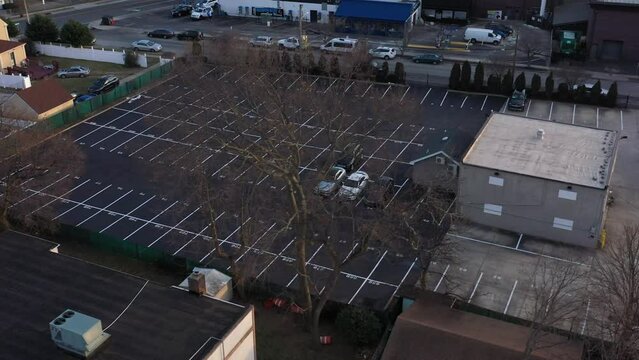 An aerial view of a car dealer storage lot at sunset. The lack of inventory in the automobile industry is due to the worldwide chip shortage. The camera truck right, pan left orbiting the empty lot.