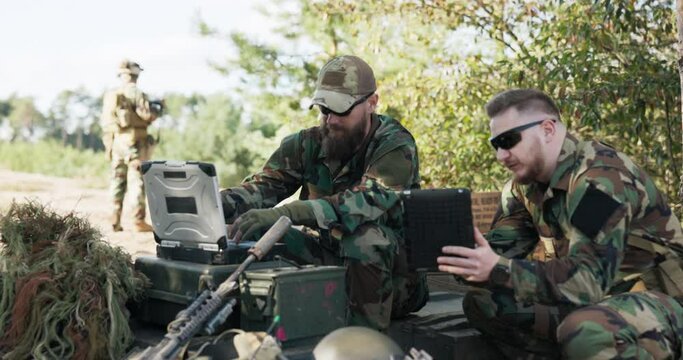 Soldiers belonging to powerful army are preparing strategy to fight surprise enemy enter data into system talk hold tablet dressed in uniforms moro, camouflage, helmets, backpacks, training ground
