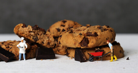 A miniature farmer dragging cart and a miniature chef with chocolate chip cookies. Miniature people and chocolate cookies with business concept.
