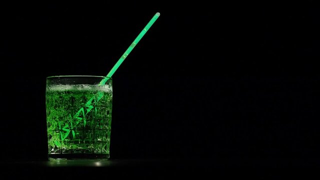 Green foaming lemonade or beer in crystal glass on a black background. Green cocktail bubbles in goblet with straw. St Patrick's Day concept. Video 4K.