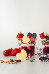Strawberry valentine's day dessert decorated with heart-shaped chocolate and ripe berries Two glasses with a sweet breakfast of cream cheese and pureed berries on a white wooden table. vertical photo